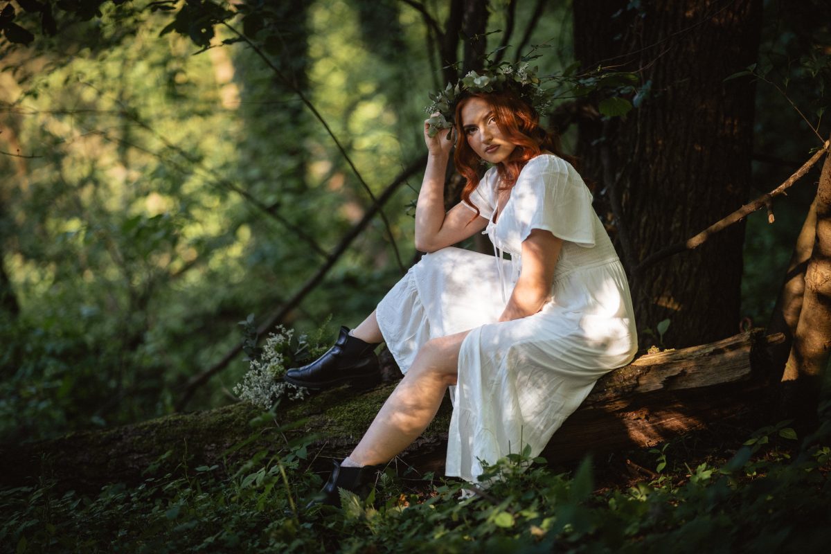 Kobieta w białej sukience siedząca na zwalonym pniu w lesie, w świetle zachodzącego słońca