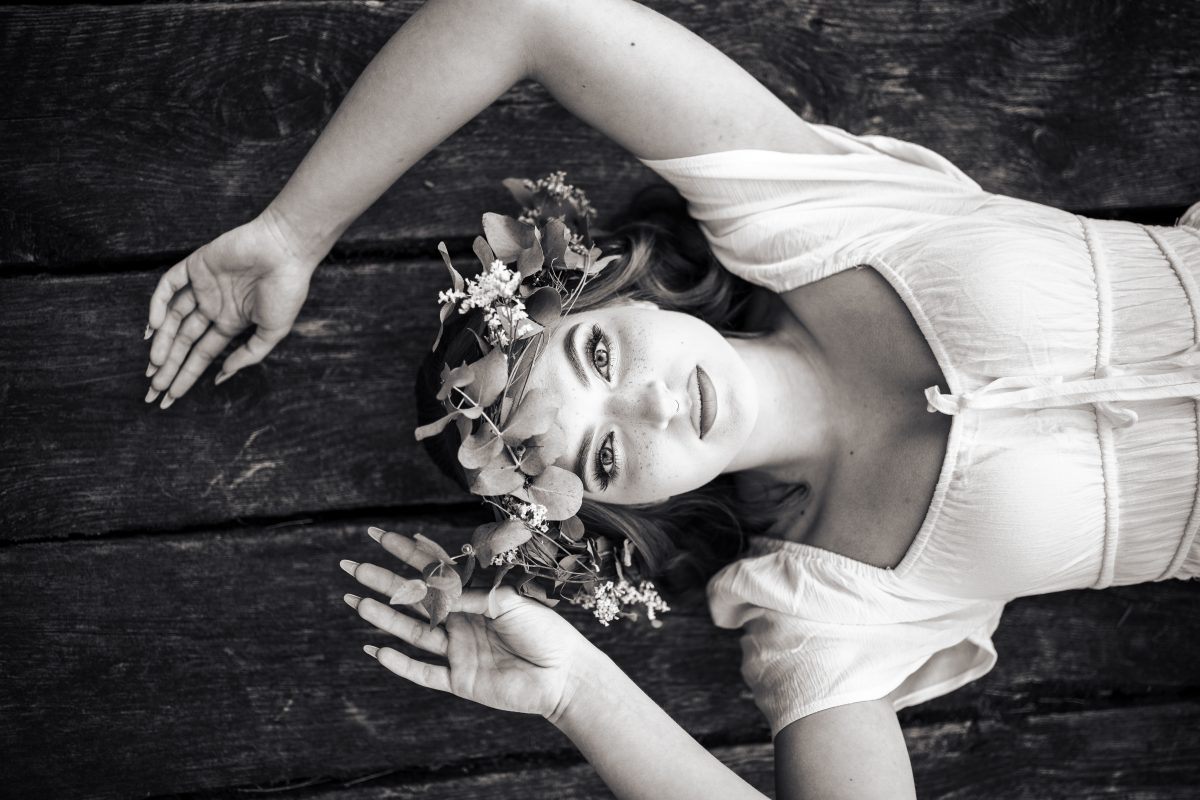 Czarnobiały portret kobiety w wianku, leżącej na drewnianym tle