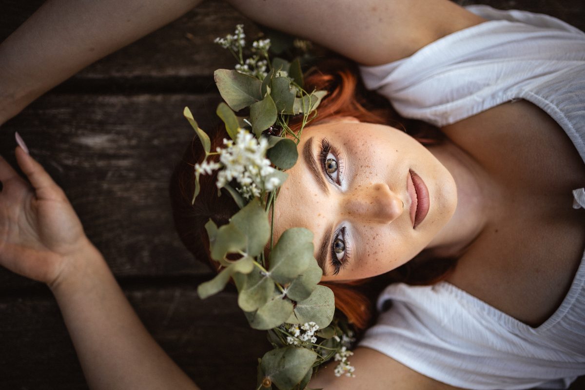 Portret kobiety w wianku z zielonych liści, leżącej na drewnianym tle