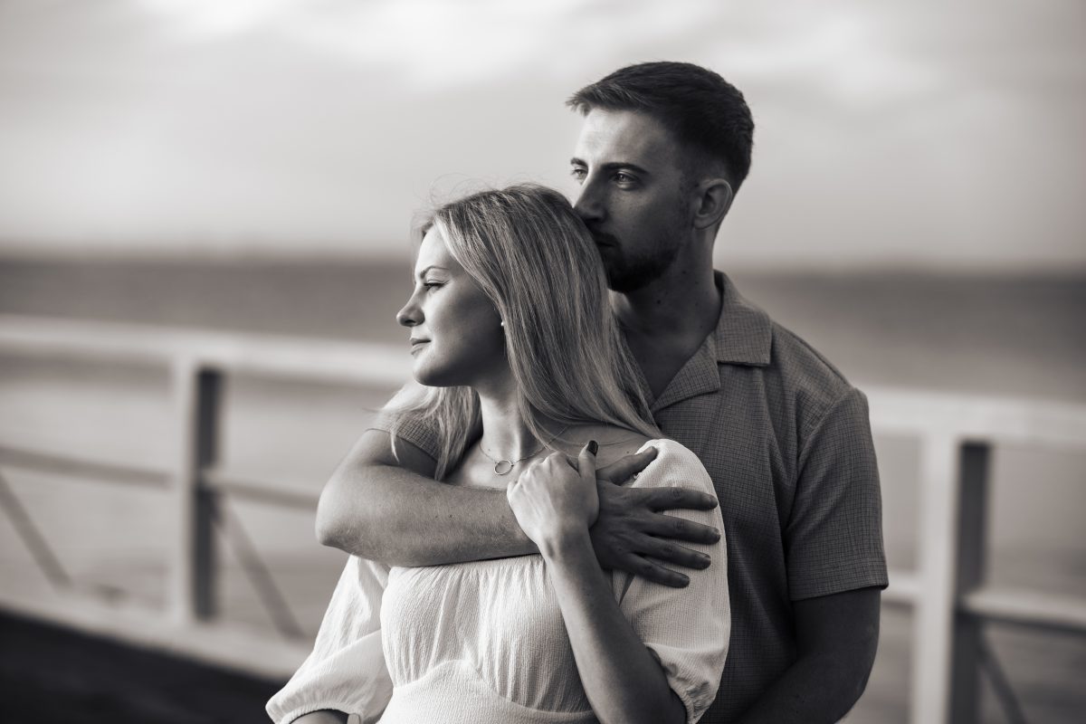 Zakochani stoją na pomoście wtulenie w siebie. Zdjęcie Czarnobiałe.