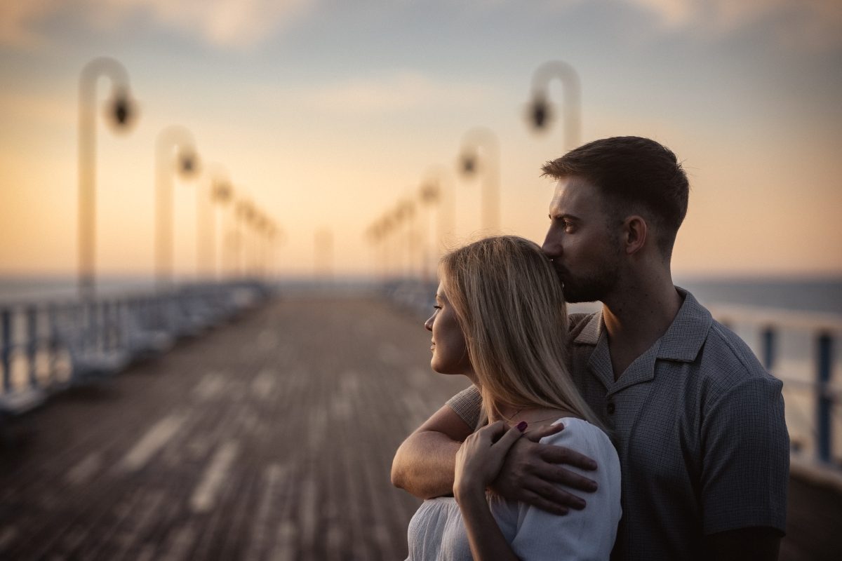 Zakochani stoją na pomoście wtulenie w siebie.