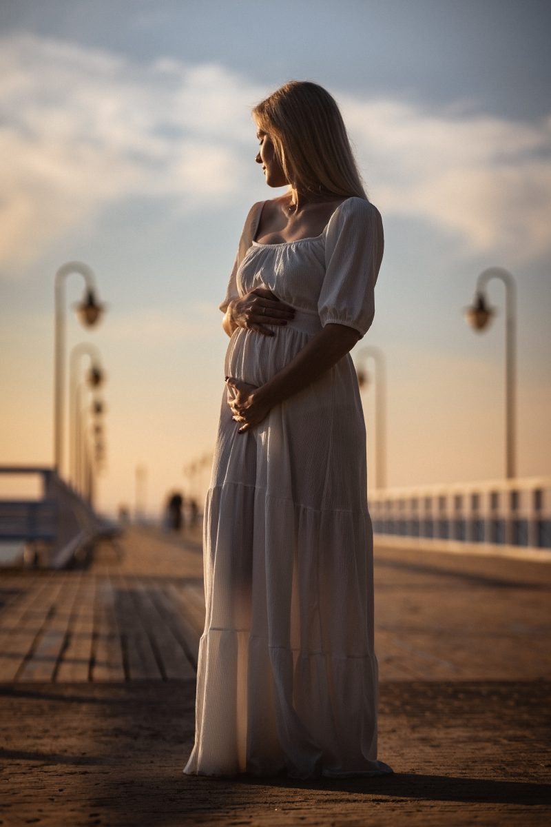 Dziewczyna w ciąży, na pomoście o wschodzie słońca.