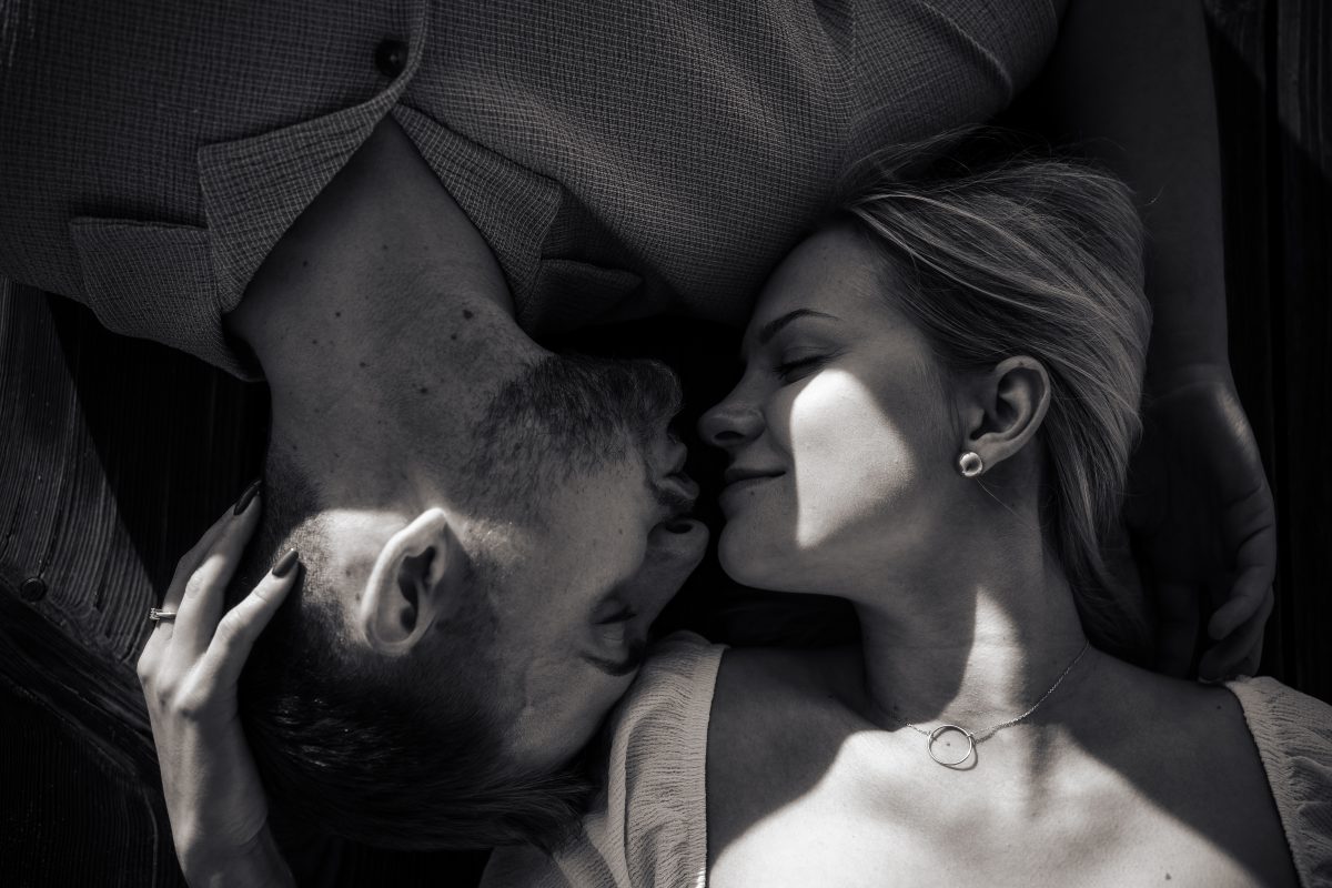 Para zakochanych leżąca na deskach pomostu w pocałunku. Zdjęcie czarnobiałe.