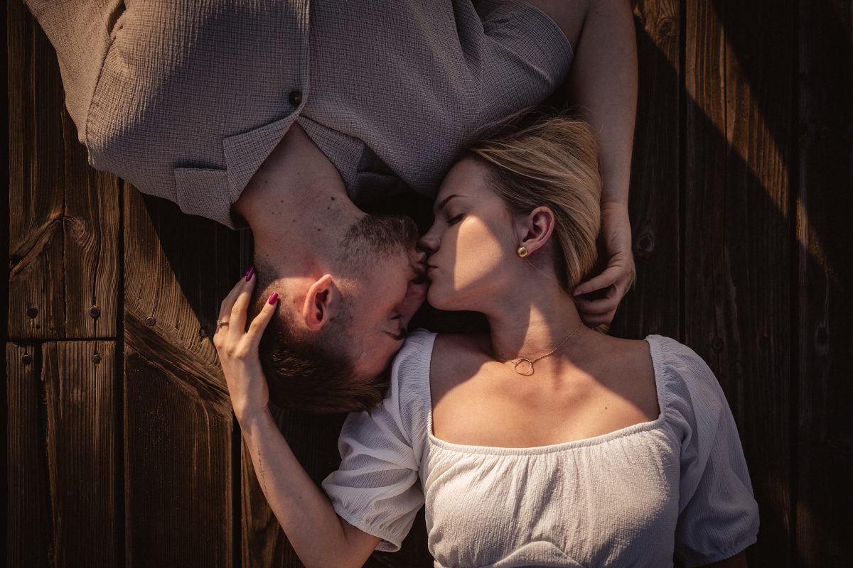 Para zakochanych leżąca na deskach pomostu w pocałunku.