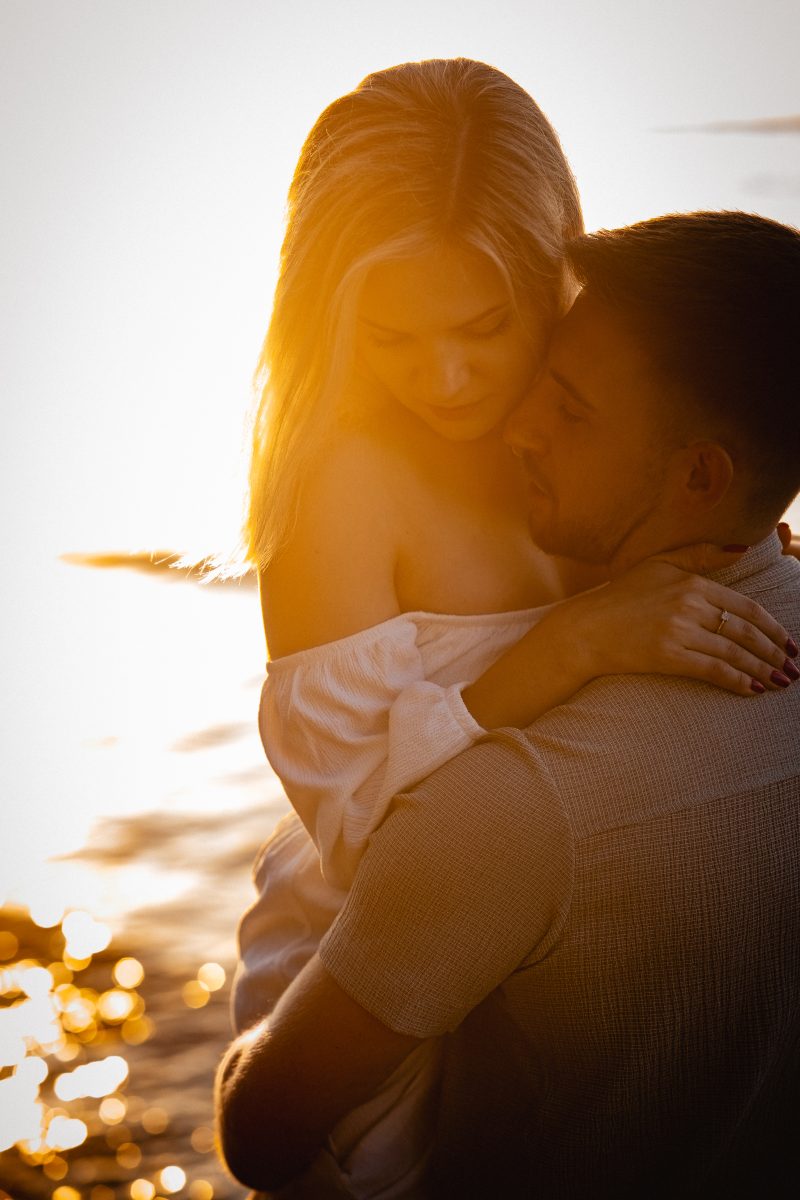 Wtulona para zakochanych na plaży, nad wodą, o wschodzie słońca.